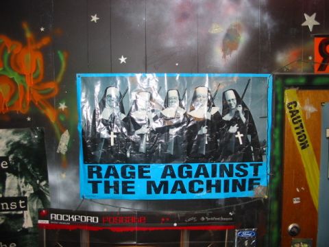 1997 Ford Crown Victoria - A poster nuns armed with rifles and the band name 'Rage Against the Machine' is displayed on a wall.