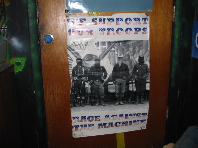 Poster showing four armed men, with text 'WE SUPPORT OUR TROOPS' and 'RAGE AGAINST THE MACHINE'