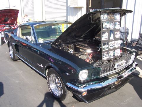 2002 Ford Mustang - A dark green classic Mustang is displayed with its hood open, revealing the engine and a collage of photographs. Another vehicle with its h…