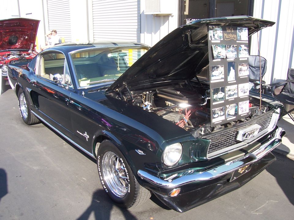 Dark green classic Mustang with hood open, displaying photo collage. Another car with red hood open visible