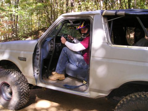 1996 Ford Bronco - A person in off-road gear sits in the driver's seat of a white Ford Bronco with the door open.