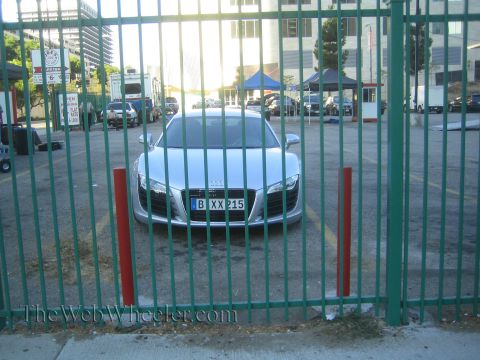 1968 Ford Mustang - A silver Audi R8 is visible through a green metal fence in a parking lot.