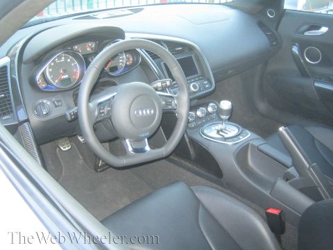 1968 Ford Mustang - The interior of a modern Audi R8 shows its dashboard, steering wheel, and gear shifter.