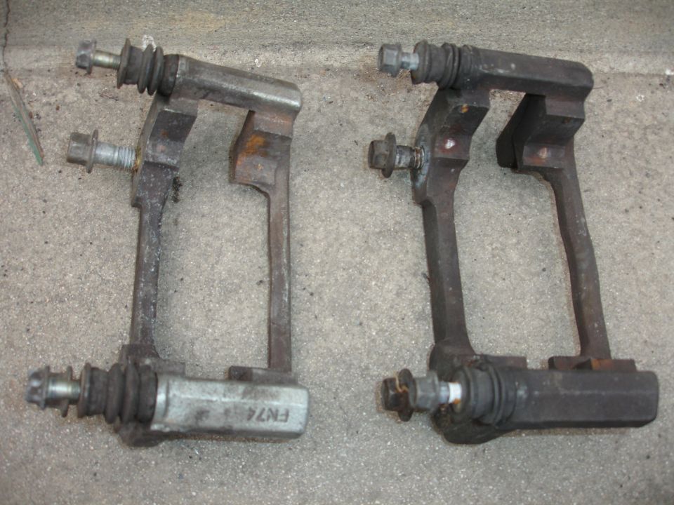 Two rusty brake caliper brackets, one with 'FN74' stamped on it, lie on a concrete surface