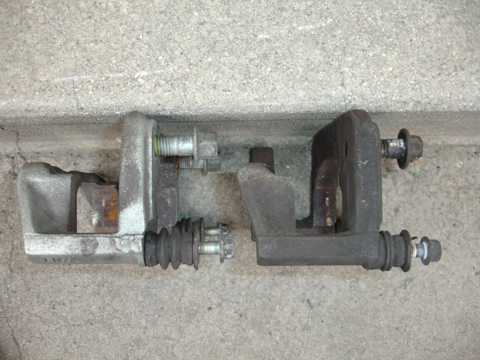 Two brake calipers, one silver and one black, resting on a concrete surface