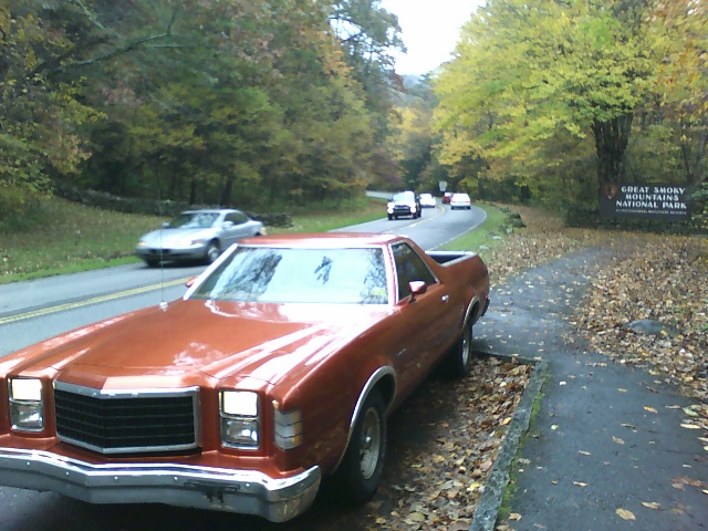 Orange Ford Ranchero parked on roadside with fall foliage and Great Smoky Mountains National Park sign
