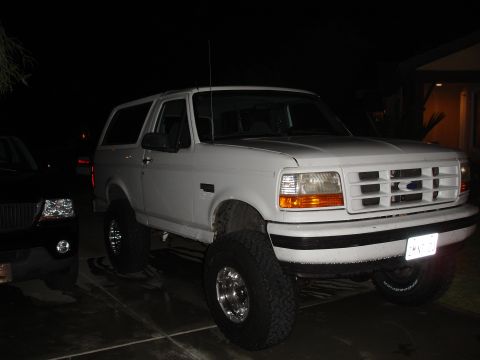 1996 Ford Bronco - This lifted 1996 Ford Bronco is parked next to another vehicle at night.