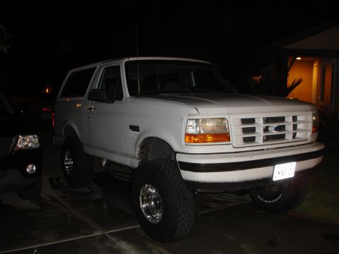 1996 Ford Bronco - White 1996 Ford Bronco with lifted suspension and aftermarket wheels is parked outside at night.