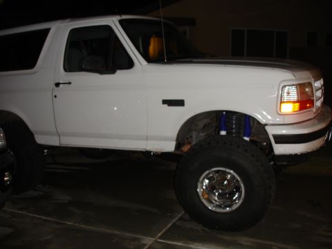 1996 Ford Bronco - A white Ford Bronco is parked at night, showing its lifted suspension and large tires.