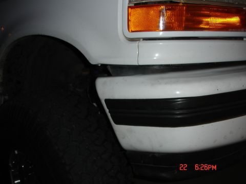 1996 Ford Bronco - Close-up of the front corner of a white 1996 Ford Bronco, showing the headlight, turn signal, and black bumper trim.