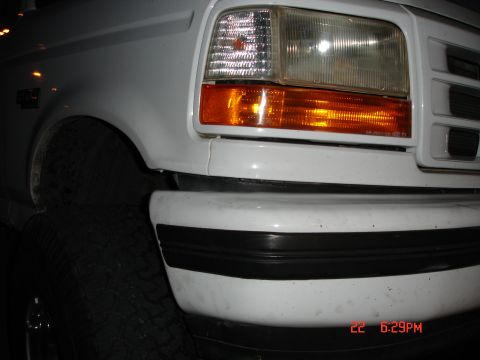 1996 Ford Bronco - Close-up of the front corner of a white 1996 Ford Bronco, showing the headlight, turn signal, and bumper.