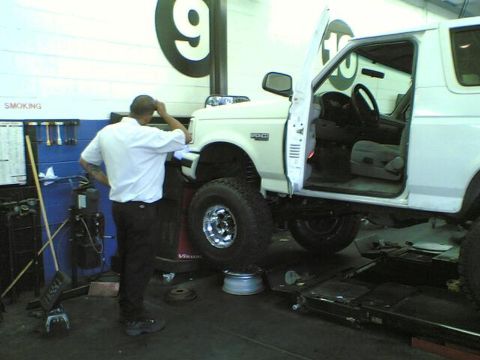 1996 Ford Bronco - Mechanic works on a 1996 Ford Bronco lifted for service in a repair shop.