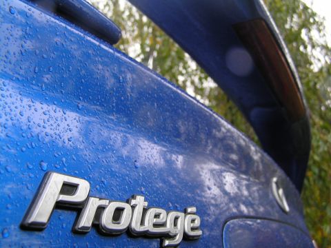 2003 Mazda Protege - Rear view of a blue 2003 Mazda Protege with water droplets on the trunk and a spoiler.