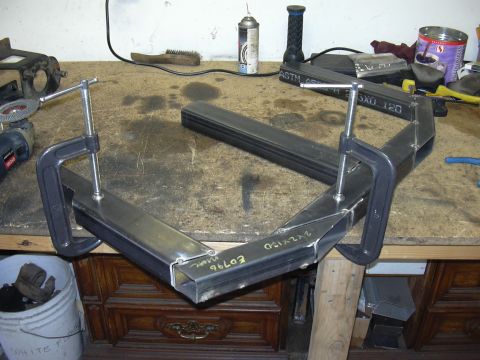 1991 Ford Bronco - A shop-built bumper or frame section tack-welded from square steel tubing, clamped together with two large C-clamps on a workbench. The tub…