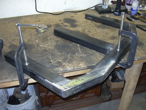 1991 Ford Bronco - A metal frame is being worked on, secured by clamps on a workbench.