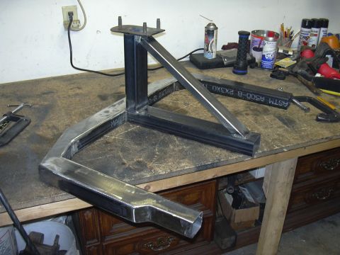 1991 Ford Bronco - A bare-steel fabricated bracket assembly made from bent and welded square tubing with a vertical post and studded top mounting plate, resti…