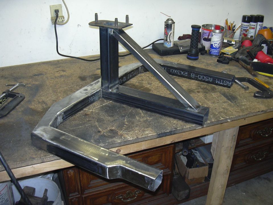 Bare steel welded tube bracket assembly with mounting plate on a garage workbench