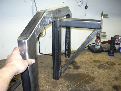 1991 Ford Bronco - A hand steadies a bare-steel fabricated frame section built from mitered and welded square tubing with a ground-smooth bend and a gusseted…