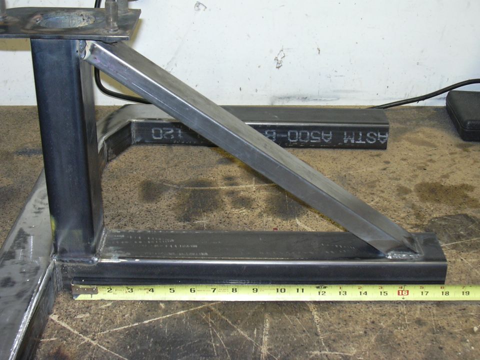Welded square steel tube bracket with diagonal brace on a workbench beside a tape measure