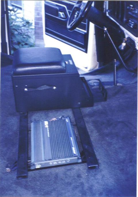 1979 Ford Bronco - An aftermarket amplifier is installed on the floor of a vehicle, next to a console with a seat.