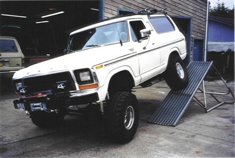 1979 Ford Bronco - Modified white Ford Bronco on a ramp in a garage setting, with another vehicle in the background.