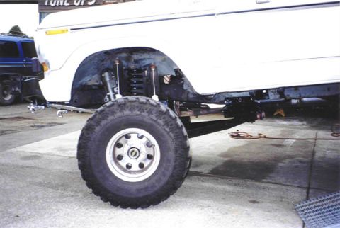 1979 Ford Bronco - The front suspension and wheel of a white SUV are shown, with another vehicle in the background.