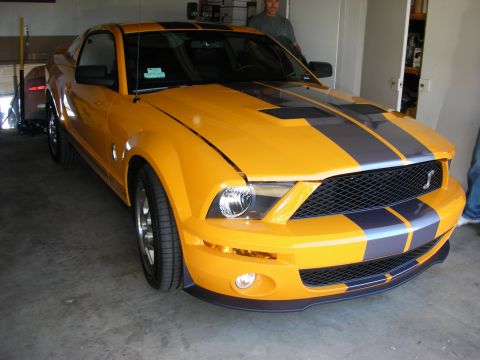 1998 Ford Crown Victoria - orange Ford Shelby GT500 Mustang with black dual racing stripes and a Cobra grille emblem sits parked in a garage with a man standing behin…