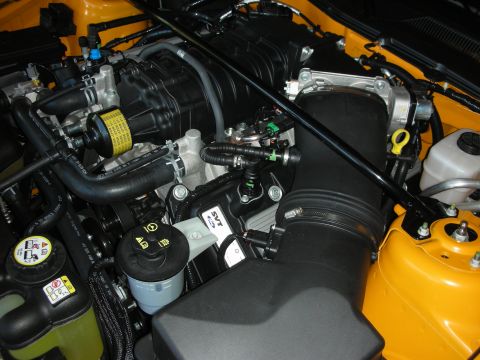 1998 Ford Crown Victoria - Detail of an engine compartment with a black oil filter, ribbed intake hose, and an SVT-branded cover against yellow painted bodywork.