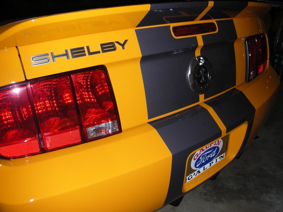 Rear of a yellow car with black stripe and chrome SHELBY lettering and round taillights