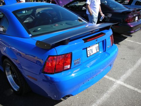 1998 Ford Crown Victoria - Rear of a blue Ford Mustang with a black rear spoiler, round taillights, and a license plate reading 32V V8.