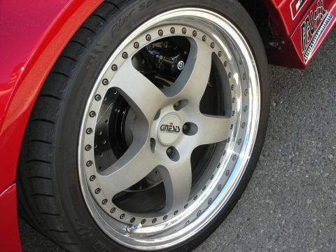 1998 Ford Crown Victoria - Detail of a polished multi-piece alloy wheel with dark spokes and a low-profile tire mounted on a red car.
