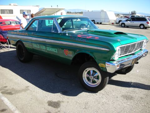 1998 Ford Crown Victoria - Green vintage Ford Falcon gasser-style drag car with a tall raised front suspension and sponsor lettering at an outdoor event.