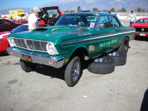 1998 Ford Crown Victoria - Green vintage Ford Falcon gasser drag car with a raised front end parked beside spare slick tires with mountains in the background.