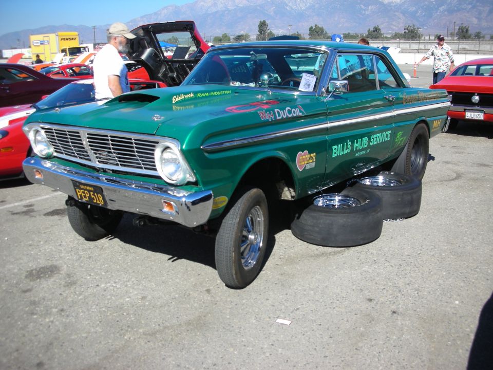 Green Ford Falcon gasser drag car parked with spare slicks beside it, mountains behind