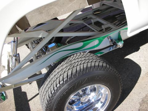 1998 Ford Crown Victoria - Close-up of a white custom truck's exposed tubular chassis and suspension with green flame paint and a chrome wheel.