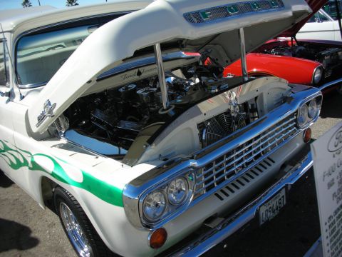 1998 Ford Crown Victoria - White vintage Ford truck with its hood raised showing the engine and radiator, green flame graphics, and FORD hood lettering.