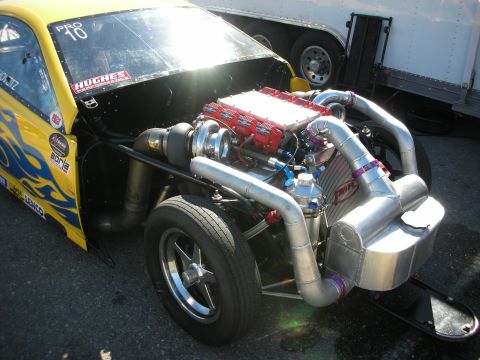 1998 Ford Crown Victoria - Yellow race car with its hood removed exposing a large turbocharged engine with red valve covers, plumbing, and an intercooler.