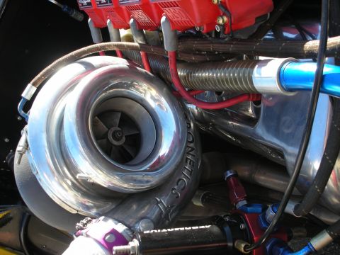 1998 Ford Crown Victoria - Close-up of a large polished turbocharger compressor wheel and housing mounted beside red valve covers and red plug wires.