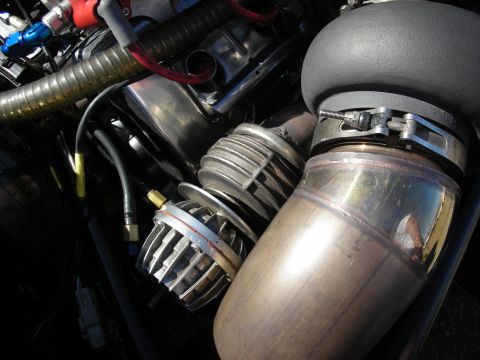 1998 Ford Crown Victoria - Detail of a chrome external wastegate and stainless exhaust piping with a black coupler on a turbocharged engine.