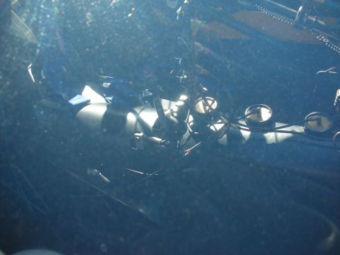 1998 Ford Crown Victoria - Dim hazy view through a glass surface showing reflective silver engine parts and round gauges, with heavy glare obscuring detail.