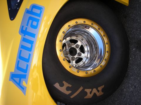 1998 Ford Crown Victoria - Yellow drag car fender bearing a blue Accufab decal above a polished Weld beadlock wheel wrapped in an M/T drag slick.