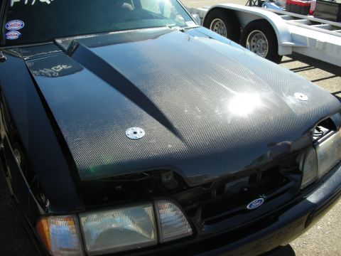 1998 Ford Crown Victoria - black Fox-body Ford with a carbon fiber hood and pin fasteners, parked beside an open trailer.