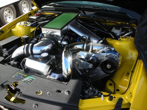1998 Ford Crown Victoria - yellow car's engine bay featuring a polished centrifugal supercharger, chrome tubing and a green air filter.