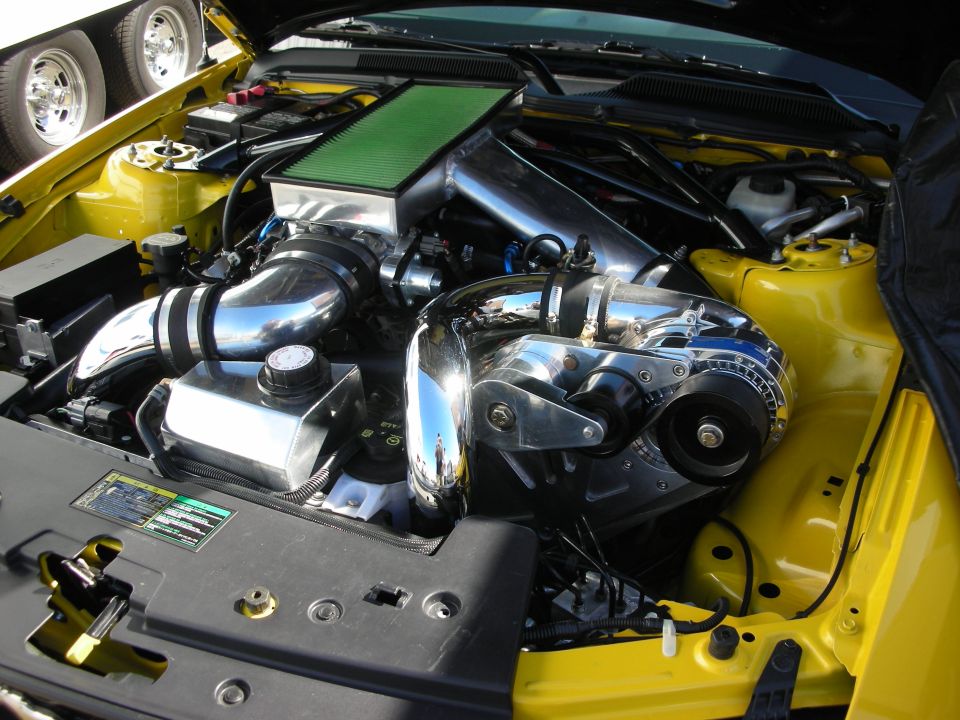 Yellow car engine bay with polished centrifugal supercharger and green filter