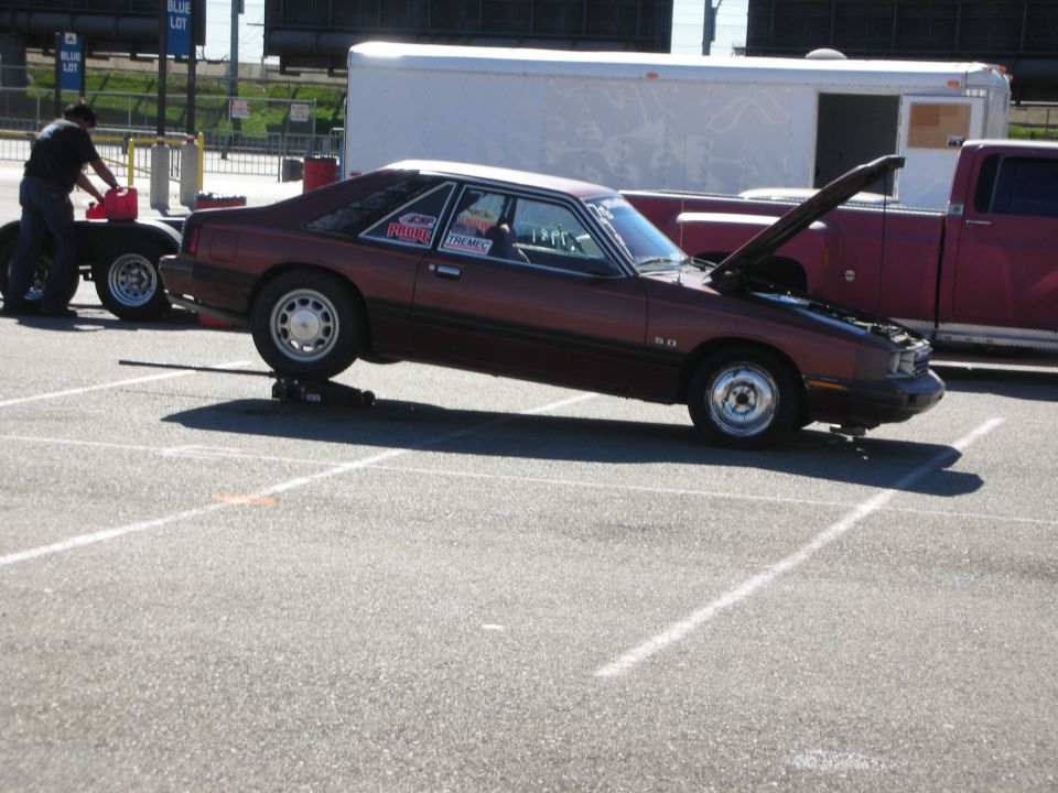 Maroon Fox-body Mercury Capri drag car on jack stands in lot