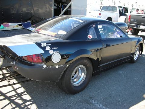 1998 Ford Crown Victoria - black New Edge Mustang drag car with a skinny front tire and Blaaker Equipment Company lettering in a pit.