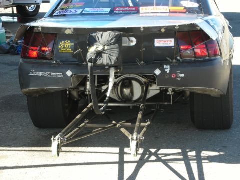 1998 Ford Crown Victoria - rear of a black drag car with bodywork showing the exposed rear axle, sponsor decals and wheelie bars.