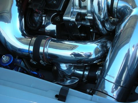 1998 Ford Crown Victoria - Close-up of polished chrome intake tubing joined by black silicone couplers and clamps over a light-blue engine bay.