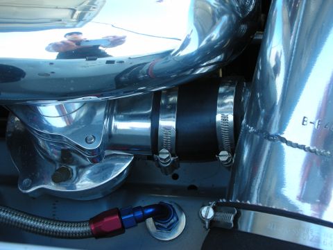 1998 Ford Crown Victoria - Polished aluminum coolant elbow connected by a black silicone hose with stainless clamps and a red-blue AN fitting nearby.