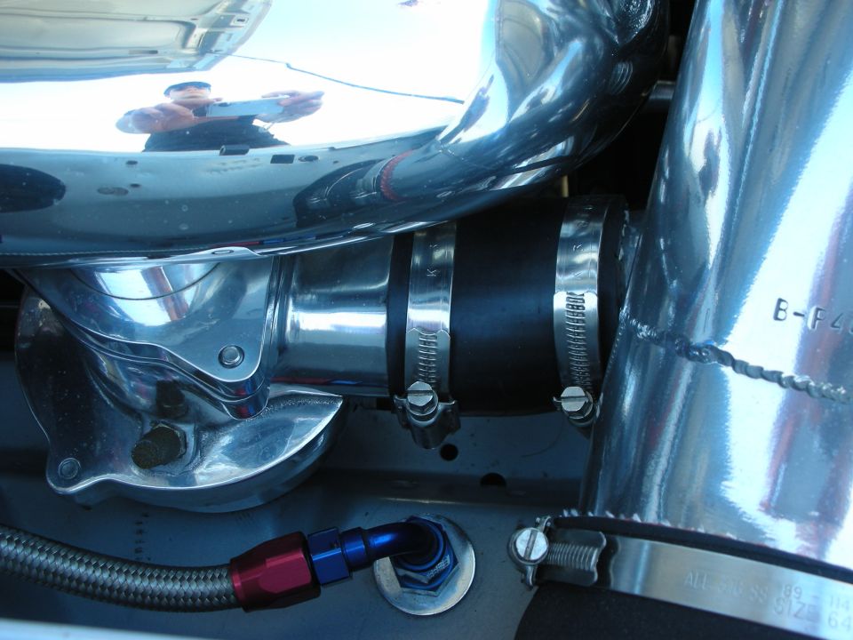 Polished metal coolant elbow with silicone hose and clamps in an engine bay